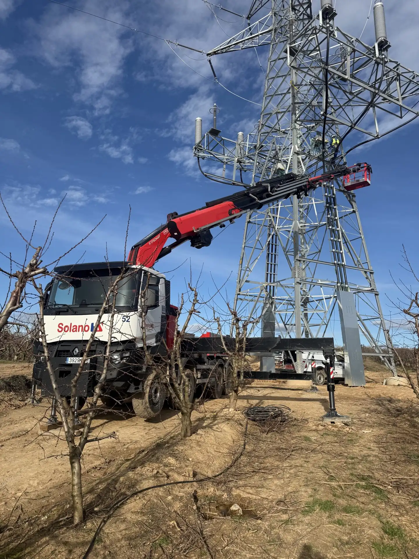 Cesta homologada elevando personas junto a una torre eléctrica